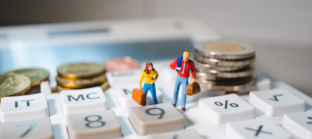 Two figurines carrying bags on a calculator with coins, representing cost of living
